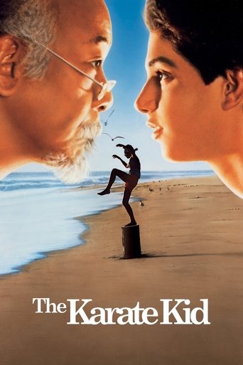 The poster features a dramatic, sunlit beach scene with two characters facing each other, one in a karate stance and the other in a relaxed pose. The warm tones of the sand and sky evoke a sense of adventure and camaraderie, while the bold title "The Karate Kid" anchors the composition.