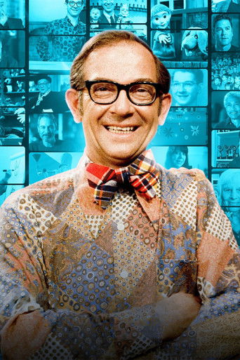The poster features a cheerful man with glasses and a plaid bow tie, surrounded by a collage of various faces and objects, all bathed in a blue hue. The playful and whimsical atmosphere suggests a magical make-believe theme.