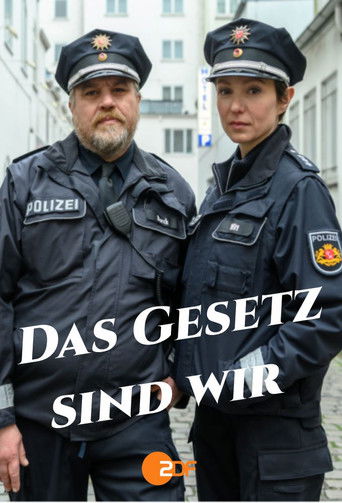 The poster features two police officers in dark uniforms with "POLIZEI" patches, standing against a backdrop of white buildings. The bold white text "DAS GESETZ SIND WIR" dominates the image, conveying a serious and authoritative tone. The overall mood is solemn and determined, reflecting the gra...
