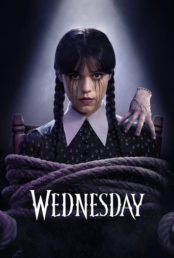 A young girl with braided hair and a nervous expression stands under a spotlight, her hands bound by thick rope. The dark, moody atmosphere with dramatic lighting creates a suspenseful mood. The title "Wednesday" appears in bold white letters at the bottom.