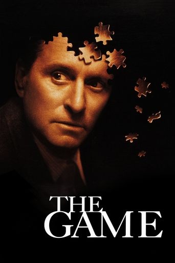 The poster features a close-up of a man's face against a dark background, with puzzle pieces floating around his head, suggesting mystery and intrigue. The title "The Game" is prominently displayed at the bottom in bold white letters, evoking themes of suspense and intellectual engagement.