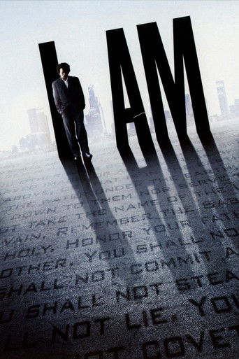 The poster features a solitary figure in a dark suit standing amidst towering, shadowy letters spelling "I AM" against a blurred cityscape. The muted tones and dramatic lighting evoke a somber, mysterious mood, suggesting themes of identity and personal struggle.
