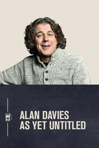 The poster features a warm, smiling Alan Davies in a textured gray sweater against a soft beige background. A dark blue strip at the bottom displays his name in bold white text, conveying a sense of understated elegance and timeless appeal.