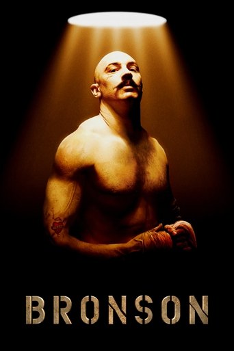 A muscular man with a mustache stands under a spotlight, bathed in warm golden light against a dark background. The poster exudes intensity and drama, with bold typography at the bottom reading "BRONSON."