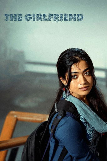 The poster features a young woman with dark hair and a blue scarf, looking directly at the viewer with a serious expression. She wears a backpack and stands against a muted, atmospheric background. The title "THE GIRLFRIEND" appears in bold, uppercase letters at the top. The overall mood is conte...