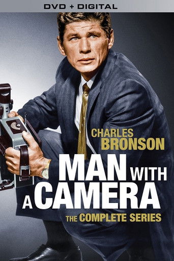 The poster features a man in a dark suit holding a camera, exuding a serious and professional mood. The bold title "Man with a Camera" dominates the center, with the actor's name highlighted above it. The color scheme uses dark tones with gold accents, creating a dramatic and intense atmosphere.