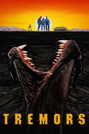 The poster features a dramatic sunset with silhouettes of three figures standing on a cliff, evoking a sense of isolation and danger. Below, a grotesque, monstrous creature with sharp teeth and a menacing posture looms over the scene, creating a suspenseful and ominous mood. The title "TREMORS" i...