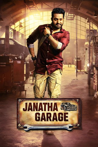 The poster features a rugged man in a red shirt and khaki pants standing confidently in a dimly lit garage. The warm, sepia-toned lighting creates an gritty, adventurous mood. The title "Janatha Garage" is prominently displayed at the bottom, hinting at a story about a man who turns his garage in...