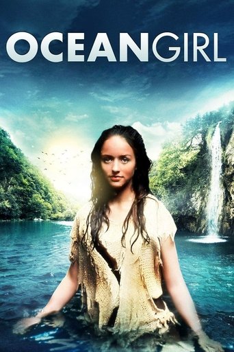 The poster features a woman with long hair standing in a serene, turquoise ocean, surrounded by lush green cliffs and a cascading waterfall. The sky is filled with soft blues and whites, creating a dreamy, peaceful atmosphere. The title "Ocean Girl" is prominently displayed at the top in bold whi...