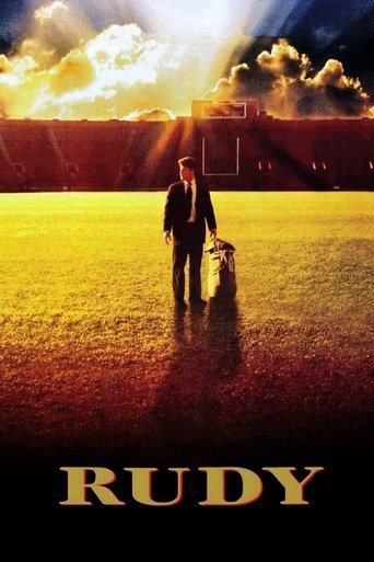 The poster features a solitary figure in a dark suit walking through a golden field under a dramatic sky filled with fiery clouds. The warm, golden hues evoke a sense of hope and nostalgia, while the silhouette of a dog adds a touch of innocence and companionship. The title "Rudy" is prominently ...