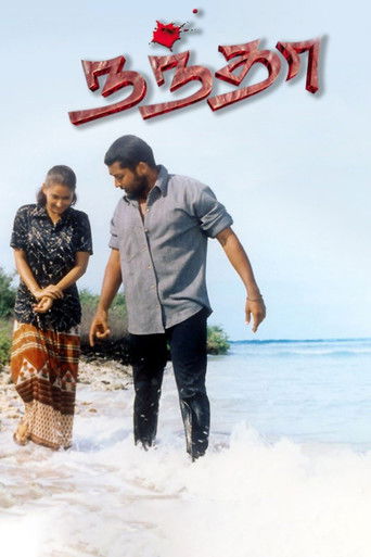 The poster features two individuals walking along a sandy beach, with the title "Nandha" prominently displayed in bold, red, stylized text. The warm tones of the sand and the ocean create a serene, romantic atmosphere, suggesting a story of love and connection.