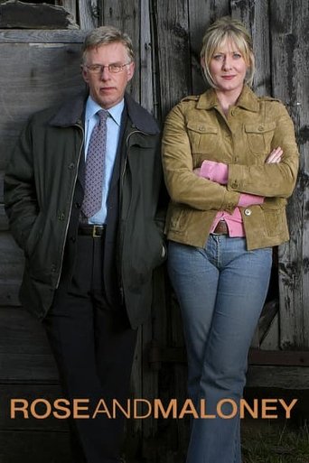 The poster features two characters standing against a weathered wooden backdrop. The man in a suit and tie exudes authority, while the woman in a mustard jacket and pink shirt appears confident and slightly mysterious. The warm tones of their clothing contrast with the muted, earthy background, c...