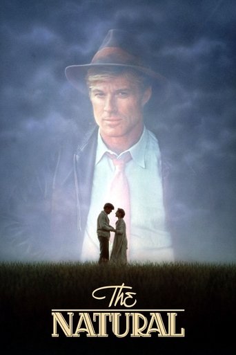 The poster features a large, ghostly figure of a man in a hat against a stormy sky, while a small couple stands in the foreground amidst tall grass. The colors are muted blues and greens, creating a somber, mysterious atmosphere. The title "The Natural" is elegantly displayed at the bottom.