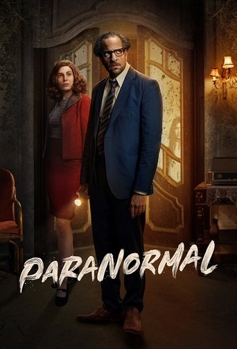 The poster features a mysterious man in a blue suit and a woman in a red dress standing in a dimly lit, eerie room. The warm glow from a window and the dark, moody atmosphere create a suspenseful mood. The title "Paranormal" is prominently displayed at the bottom, hinting at the show's supernatur...