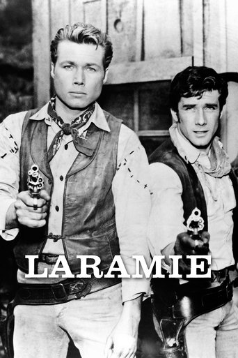 Two rugged cowboys stand against a rustic backdrop, exuding a Western charm. The sepia-toned image captures a timeless mood, with the title "LARAMIE" prominently displayed in bold, white letters.
