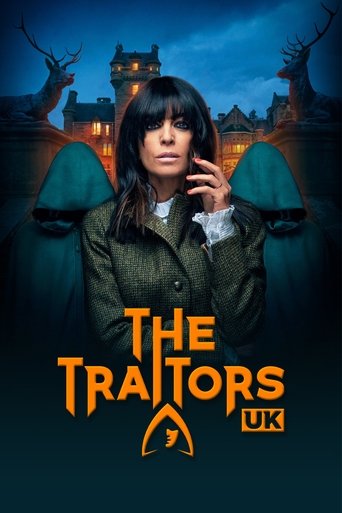 The poster features a woman with dark hair and a serious expression, surrounded by eerie, shadowy figures. The background showcases a spooky haunted house at night, illuminated by warm lights against a dark blue sky. The title "The Traitors" is prominently displayed in bold orange letters, with t...
