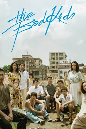 The poster features a group of diverse young people in casual attire, sitting and standing in front of a backdrop of colorful buildings. The vibrant blue title text "The Bad Kids" stands out against the sky, suggesting a lively, possibly comedic tone. The overall mood is relaxed and youthful, cap...