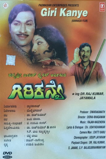 The poster features a vibrant orange background with a man and woman embracing warmly, while another actor waves cheerfully. The title "Giri Kanye" is prominently displayed in bold green letters, accompanied by a list of credits. The overall mood is warm and inviting, suggesting a romantic or com...