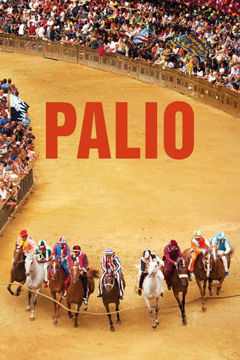 A vibrant horse race unfolds in a bustling arena, with spectators filling the stands under bright stadium lights. The scene captures the excitement of the event, with colorful jockeys and horses galloping across the sandy track. The bold red text "PALIO" dominates the image, emphasizing the event...