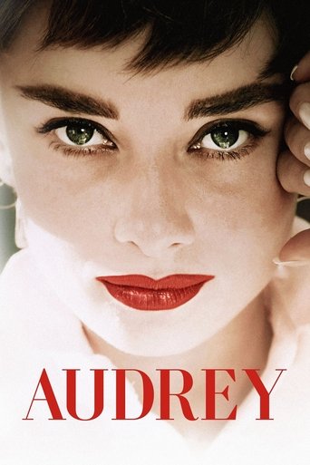 The poster features Audrey Hepburn's striking face, with bold red lips and expressive green eyes. The warm lighting and soft skin tones evoke a timeless, elegant mood. The bold red text "AUDREY" anchors the image, emphasizing the iconic star.