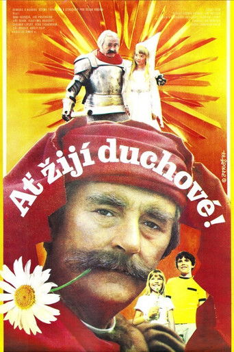 The poster features a central figure with a mustache and beard, surrounded by vibrant red and yellow hues radiating outward. Atop his head are two figures in armor and a white robe, while smaller characters appear at the bottom. The text "Ať žijí duchové!" translates to "Live the spirits!" in Cze...