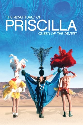 The poster features three women in vibrant desert costumes against a backdrop of a desert landscape. Their colorful outfits, including red, blue, and yellow, stand out against the sandy terrain. The mood is adventurous and whimsical, capturing the spirit of the desert.