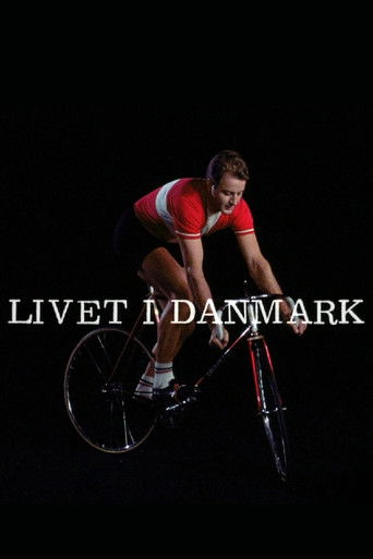 The poster features a cyclist in a red and white outfit against a stark black background, conveying a sense of motion and determination. The bold white text "LIVET IN DANMARK" anchors the image, emphasizing the film's theme of life in Denmark.
