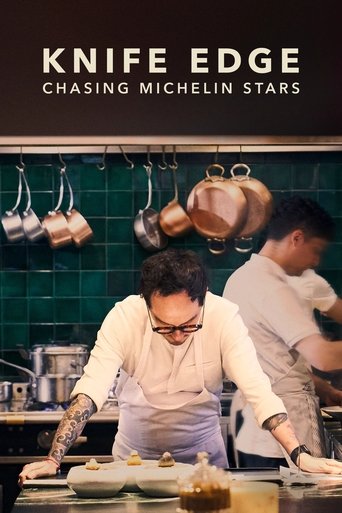 The poster features two chefs in white aprons, one with a tattooed arm and glasses, working intently over a counter. The background showcases a green-tiled wall with hanging copper pots, creating a vibrant, industrial kitchen atmosphere. The warm lighting and focused expressions convey a sense of...