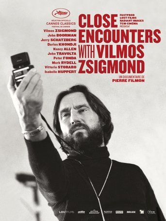 The poster features a man with a beard and long hair holding a small black object aloft, exuding mystery and intrigue. The muted tones of the image, combined with the bold red text, create a suspenseful and dramatic atmosphere.