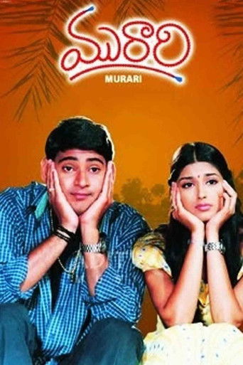 The poster features a young man and woman with hands resting on their cheeks, exuding a playful yet slightly apprehensive mood. The warm orange background with palm leaves adds a tropical ambiance, while the title "Murari" in bold red script suggests a vibrant and engaging story.
