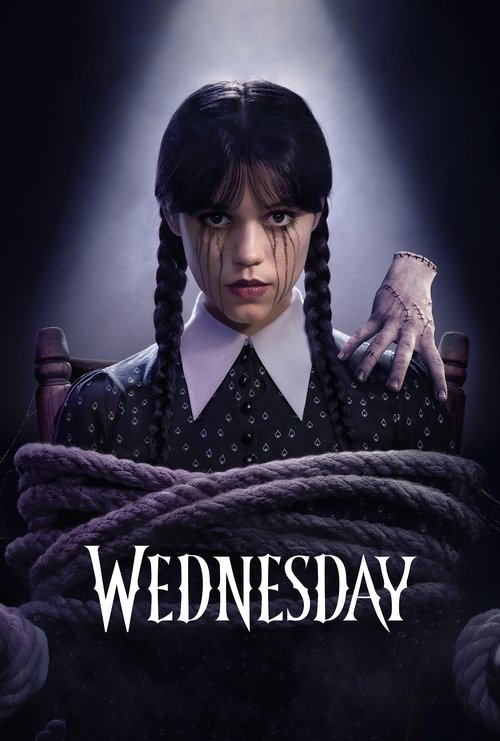 A young girl with braided hair and a nervous expression stands under a spotlight, her hands bound by thick rope. The dark, moody atmosphere with dramatic lighting creates a suspenseful mood. The title "Wednesday" appears in bold white letters at the bottom.