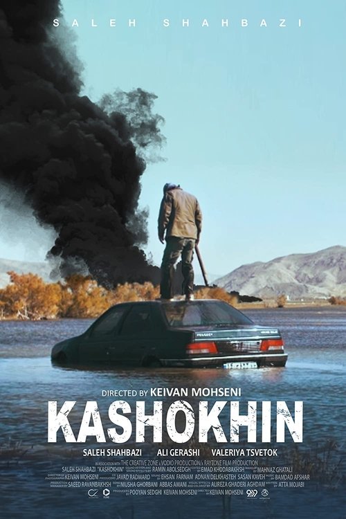 The poster features a lone figure standing atop a car, surrounded by thick black smoke against a hazy, muted landscape. The warm autumnal tones of the background contrast with the cool blues and greys of the sky and water. The title "Kashokhin" dominates the bottom, suggesting a story about displ...