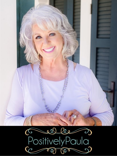 An elderly woman with gray hair smiles warmly at the camera against a backdrop of dark shutters. She wears a light purple top and a long necklace, exuding a cheerful and approachable vibe. The poster features elegant gold lettering, suggesting a positive and uplifting theme for the TV show.
