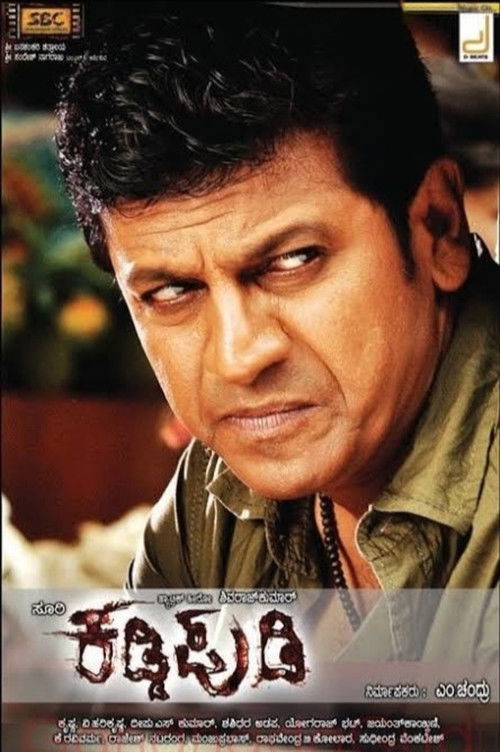 The poster features a close-up of actor Rajkumar Sharma with intense, serious eyes, set against a muted, earthy background. The title "Kaddi Pudi" is prominently displayed in bold, stylized red and gold lettering, evoking a sense of drama and nostalgia. The overall composition conveys a somber ye...