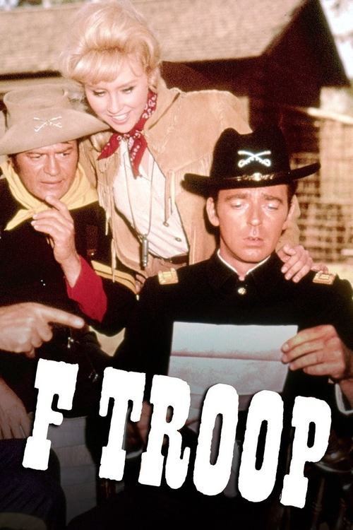 The poster features three characters in a vintage military setting, with warm tones and a nostalgic atmosphere. The central figure holds a document, suggesting a serious mission, while the others look on with concern. The bold text "F TROOP" anchors the image, emphasizing the show's gritty, histo...