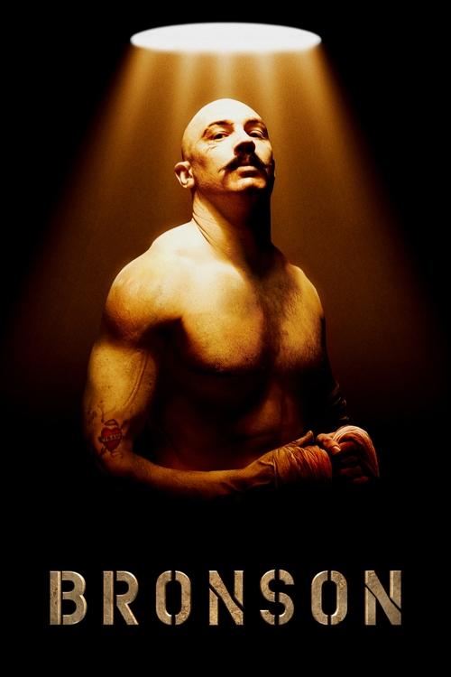 A muscular man with a mustache stands under a spotlight, bathed in warm golden light against a dark background. The poster exudes intensity and drama, with bold typography at the bottom reading "BRONSON."