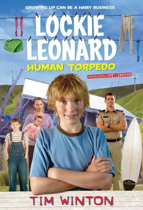 The poster features Lockie Leonard, a young man with red hair and a blue shirt, standing confidently with arms crossed. Behind him, three other characters are visible in a rural setting with green fields and a white surfboard. The background includes laundry hanging and a blue sky, suggesting a s...