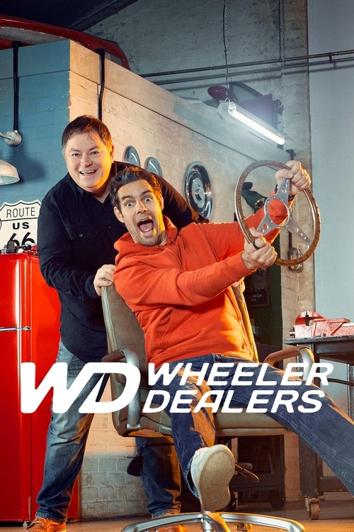 A humorous scene featuring two men in a workshop setting, one in a red sweater and the other in a dark jacket, holding a large wheel. The warm lighting and casual atmosphere convey a lighthearted, comedic mood typical of the show's quirky humor.