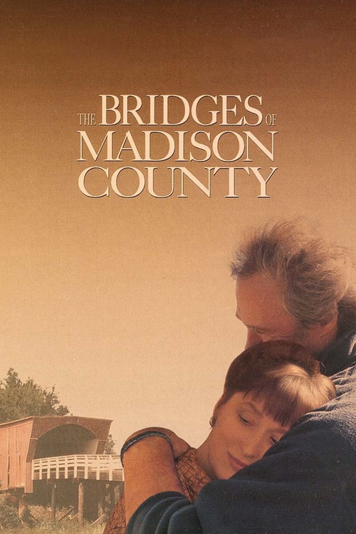 The poster features a tender embrace between an older man and a young woman, set against a warm, golden sunset. The title "The Bridges of Madison County" is elegantly displayed in serif font, evoking a sense of nostalgia and connection. The muted earth tones and soft lighting create a peaceful, r...