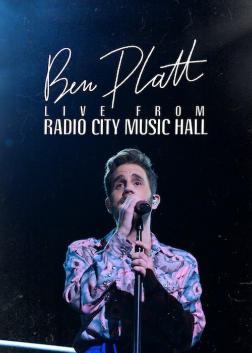 The poster features a man in a colorful, patterned shirt performing on stage, holding a microphone. The dark background emphasizes the vibrant colors of his outfit and the spotlight. The text announces his live performance at Radio City Music Hall.