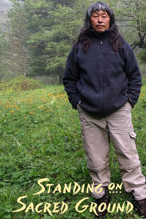 A man stands solemnly in a lush green field, surrounded by vibrant orange flowers. His dark hoodie and khaki pants contrast with the earthy tones, evoking a sense of reverence and tranquility. The serene outdoor setting and his thoughtful expression convey a peaceful, spiritual atmosphere.
