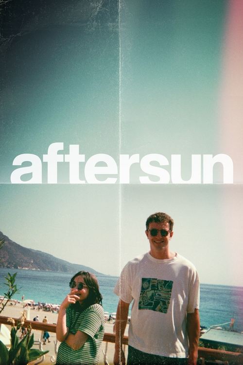 The poster features a couple standing by the ocean, with the title "Aftersun" prominently displayed in bold white letters. The warm sunset hues blend into the cool blue sky, creating a serene and romantic atmosphere.