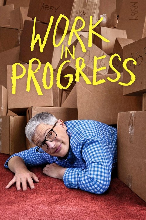 The poster features a man with glasses and a blue checkered shirt lying on his stomach on a red carpet, surrounded by cardboard boxes. The bold yellow text "WORK IN PROGRESS" dominates the top, conveying a sense of creativity and unfiltered ambition. The overall mood is energetic and inspiring, s...