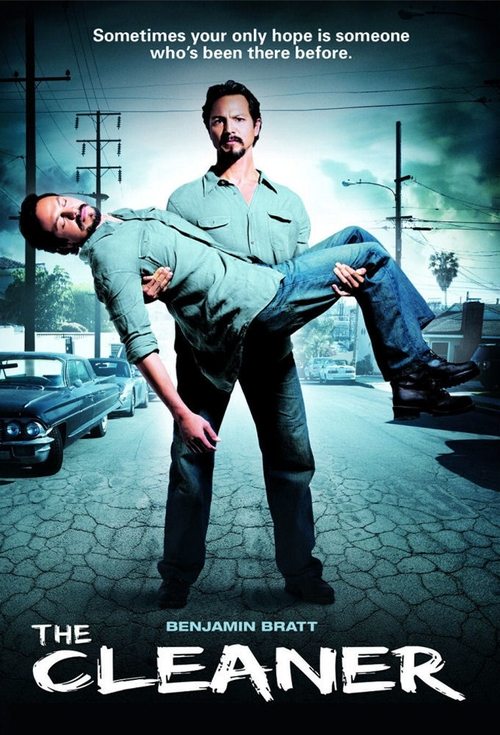 The poster features a man in a green uniform carrying another man, set against a gritty urban backdrop with a car and building. The muted tones and shadowy figures evoke a somber, tense mood, hinting at the gritty reality of the show.
