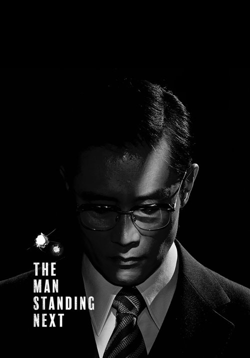 The dark, moody poster features a man in a sharp suit and glasses, exuding mystery and authority. The stark black background contrasts with the subtle glow of his face, creating an intense and suspenseful atmosphere. The title, "The Man Standing Next," hints at a thriller or drama with a dramatic...