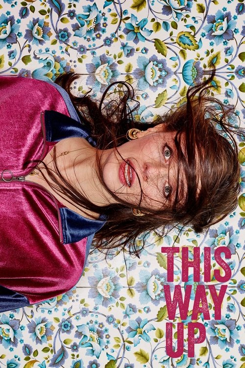 A woman with tousled brown hair lies on a floral-patterned bed, wearing a vibrant pink and blue zip-up jacket. Her expressive eyes and slightly tousled hair convey a sense of casual confidence and relaxed mood. The bold pink text "THIS WAY UP" anchors the image, suggesting a stylish and modern na...