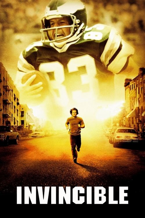The poster features a towering football player in a gold uniform with the number 33, surrounded by intense golden light that casts a dramatic glow over the scene. Below, a smaller figure runs toward the viewer, creating a sense of urgency and action. The bold, white text "INVINCIBLE" anchors the ...