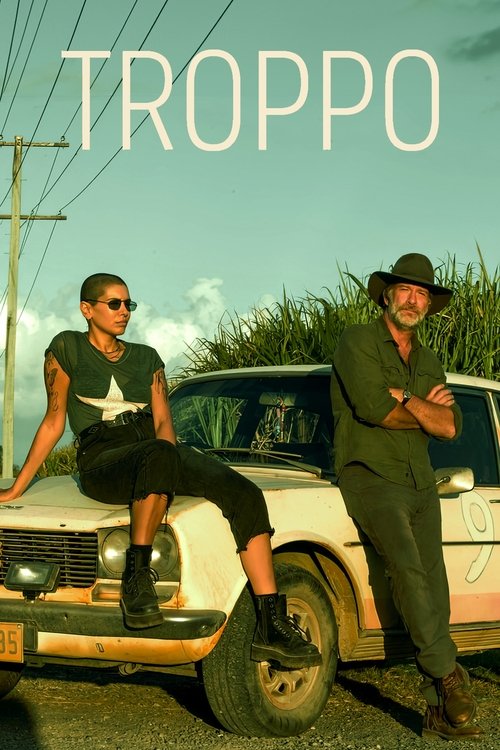 The poster features two men posing confidently against a vintage car, with the title "TROPPO" prominently displayed in bold white letters. The man on the left wears sunglasses and a black shirt with a white star, while the man on the right sports a hat and a green outfit. The scene exudes a rugge...