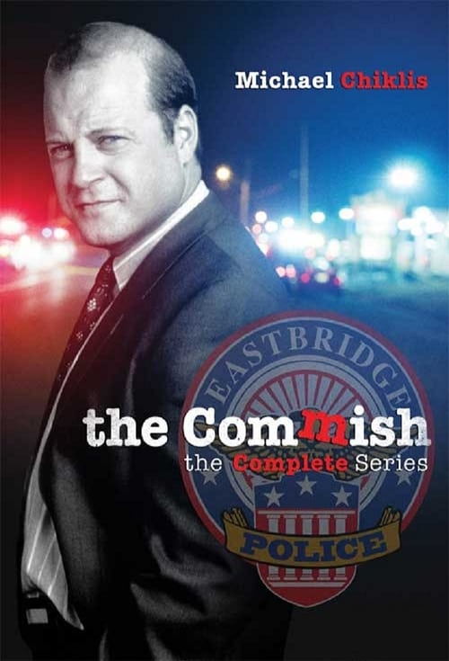 The poster features a close-up of Michael Shikil in a dark suit against a blurred, vibrant cityscape at night. The warm red and blue hues create a dramatic atmosphere, while the title "The Commish" and police badge emblem suggest a serious, high-stakes police drama.