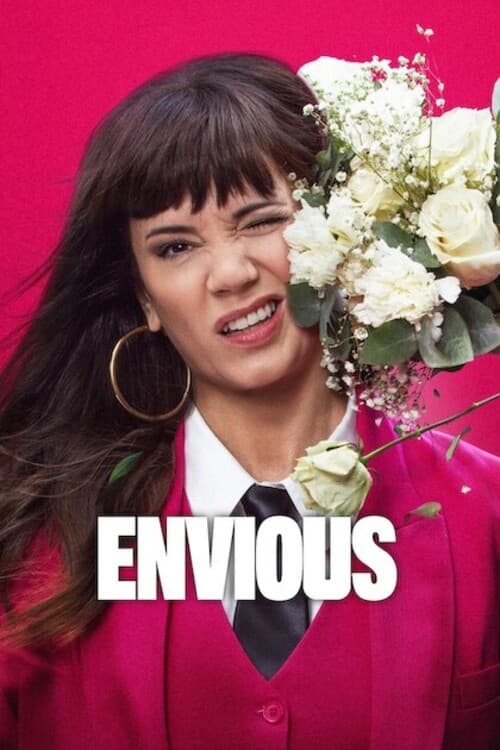 A woman with dark hair and large hoop earrings holds a bouquet of white flowers against a vibrant pink background. Her expression is playful, with a mischievous grin. The word "ENVIOUS" is prominently displayed in bold white letters across her chest.